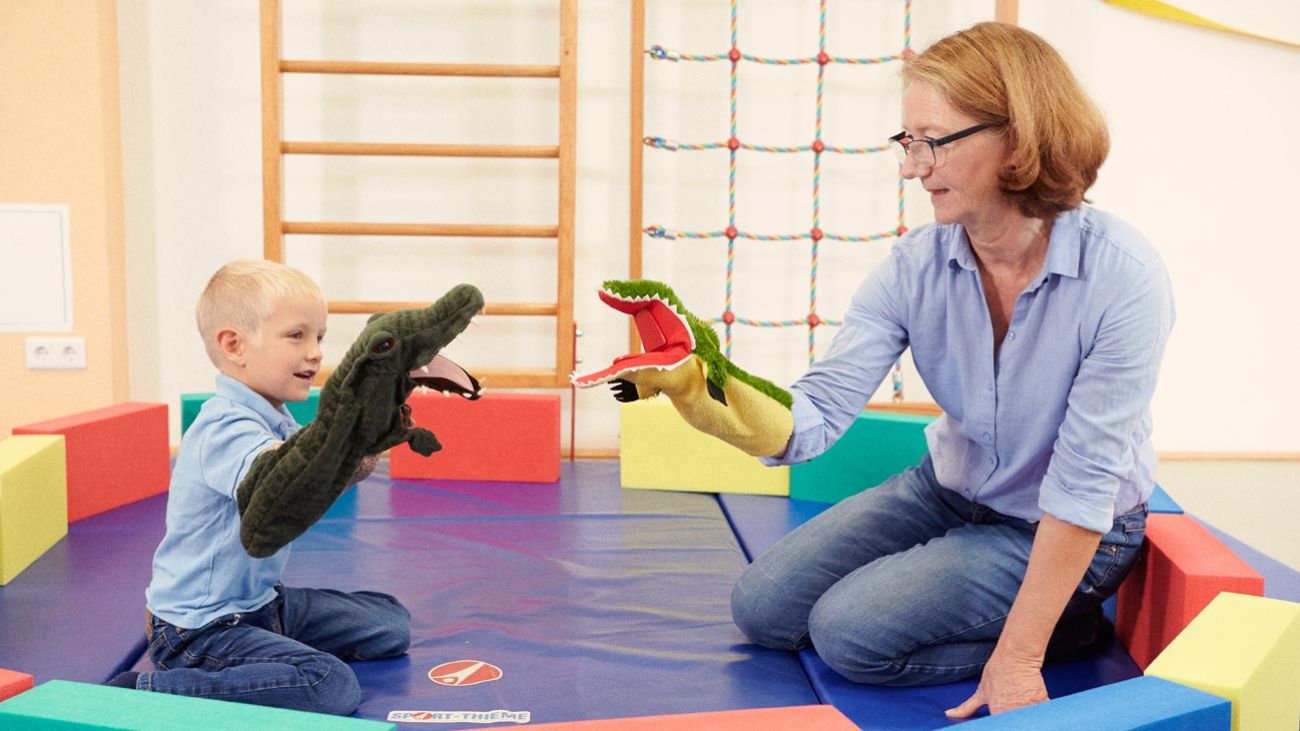 Eine Frau spielt mit einem kleinen Jungen mit Handpuppen (Krokodile).